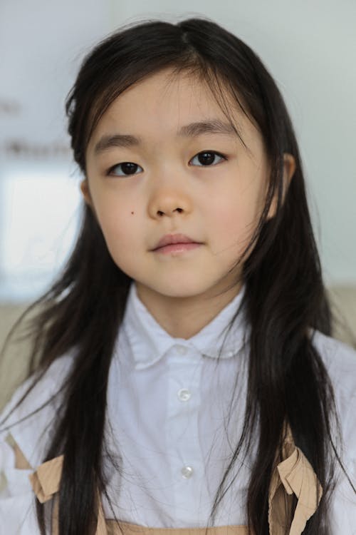 Free Portrait of charming ethnic little girl with dark hair sitting at home and looking at camera Stock Photo