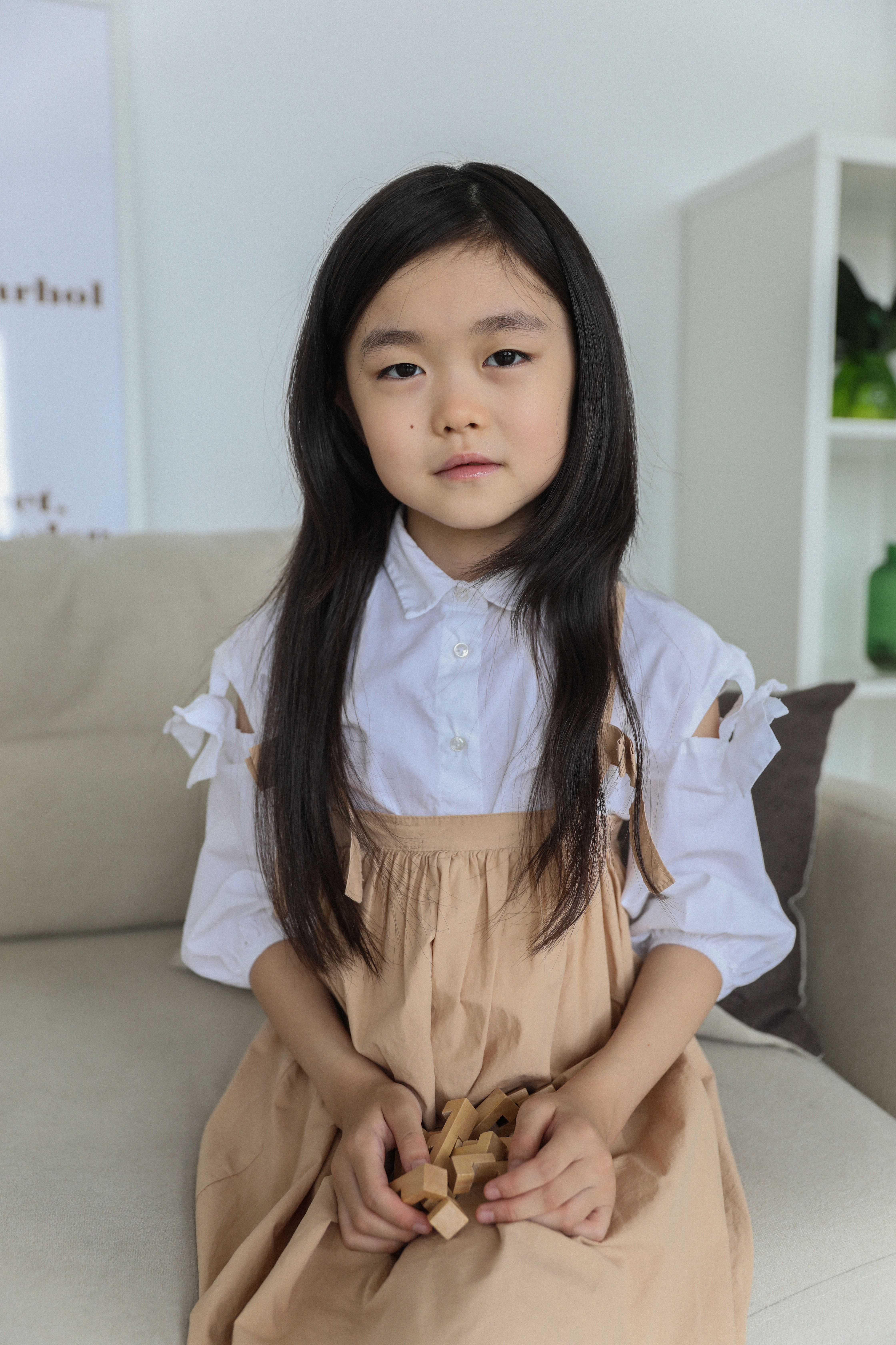 Cheerful ethnic child in trendy clothes sitting on sofa with wooden blocks and looking at camera