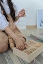 Crop faceless little girl in casual clothes sitting on floor and playing with wooden blocks