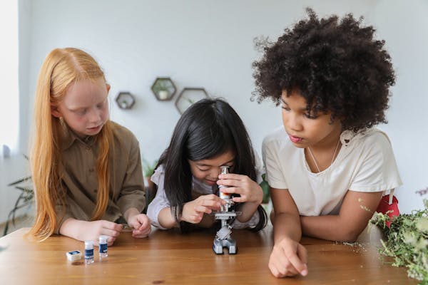 kids gather around table looking through microscope