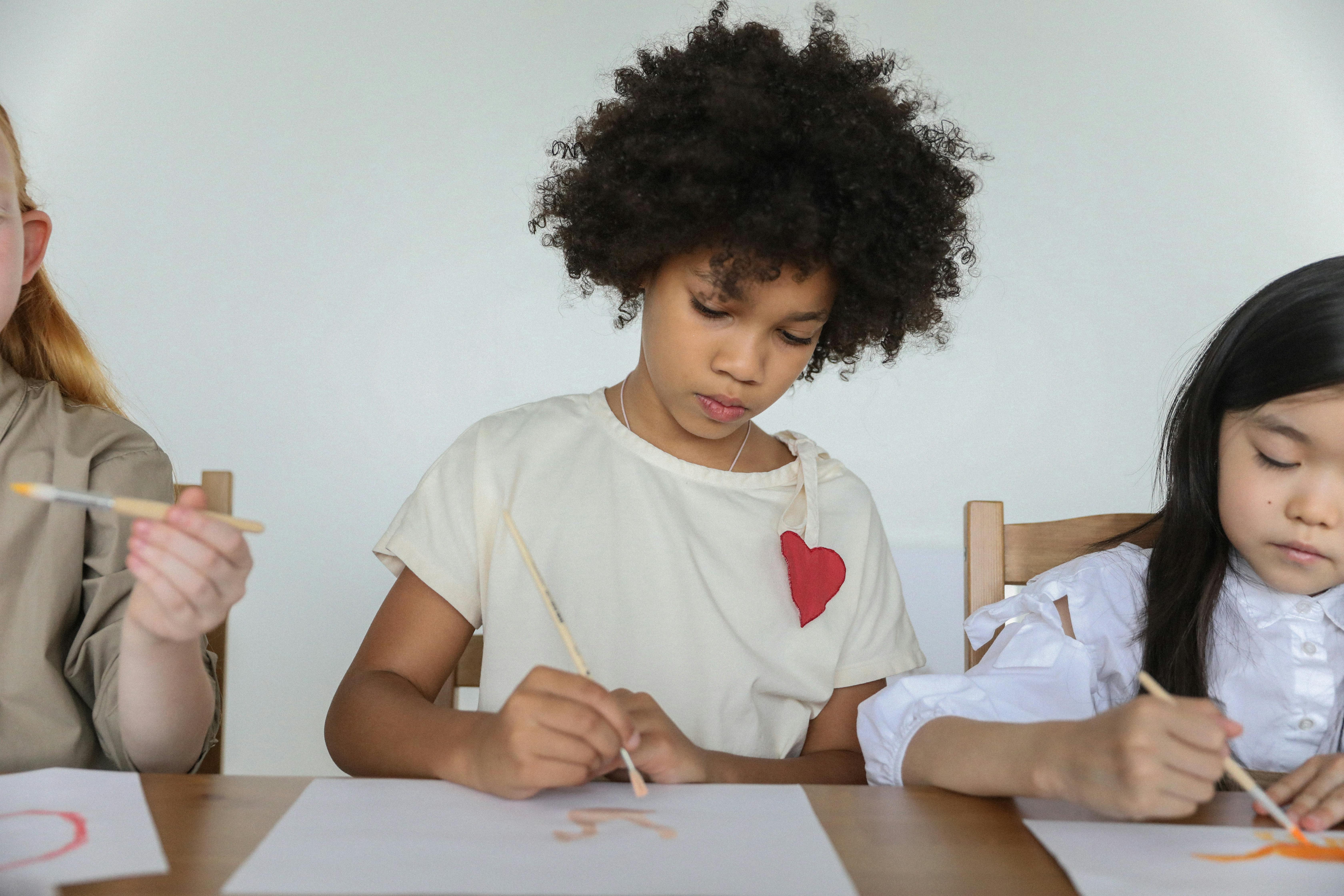 focused diverse little girls painting with brushes in art studio