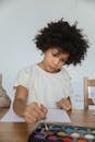 Focused African American child dipping brush in watercolor before painting