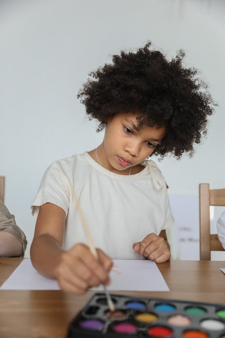 Focused African American Child Dipping Brush In Watercolor Before Painting