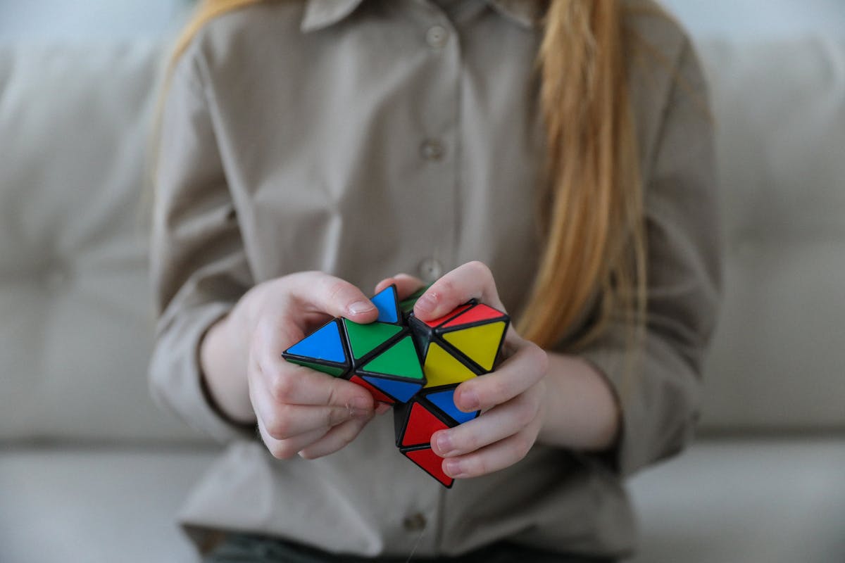Crop anonymous girl demonstrating and solving colorful puzzle with triangles in soft focus