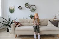 Serious girl in fashionable clothes solving puzzle and sitting on cozy sofa with bright cushion in contemporary lounge