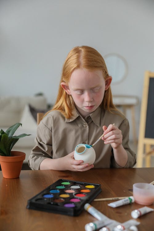 Focused cute girl decorating vase with watercolor