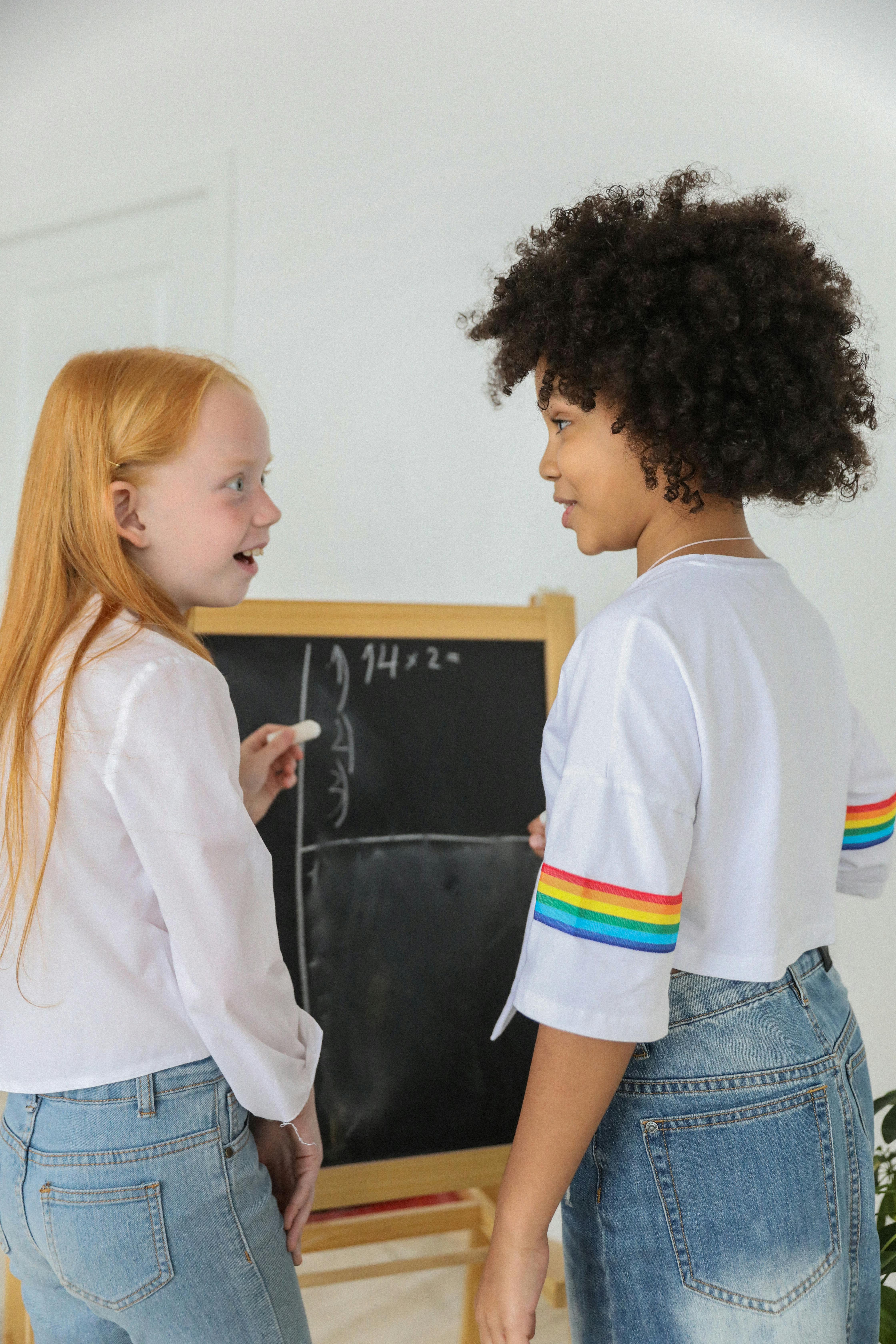 excited diverse girls in denim near chalkboard