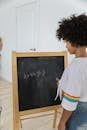 Back view of African American girl writing numbers and symbols on chalkboard in classroom