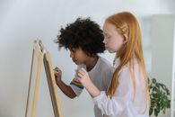 Calm multiracial girls painting on easel chalkboard