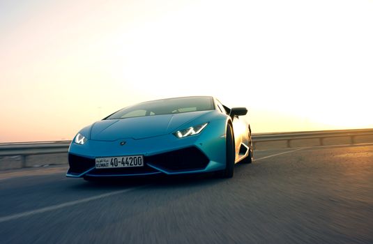Stunning blue Lamborghini Huracan on an open road during sunset, exuding luxury and speed.