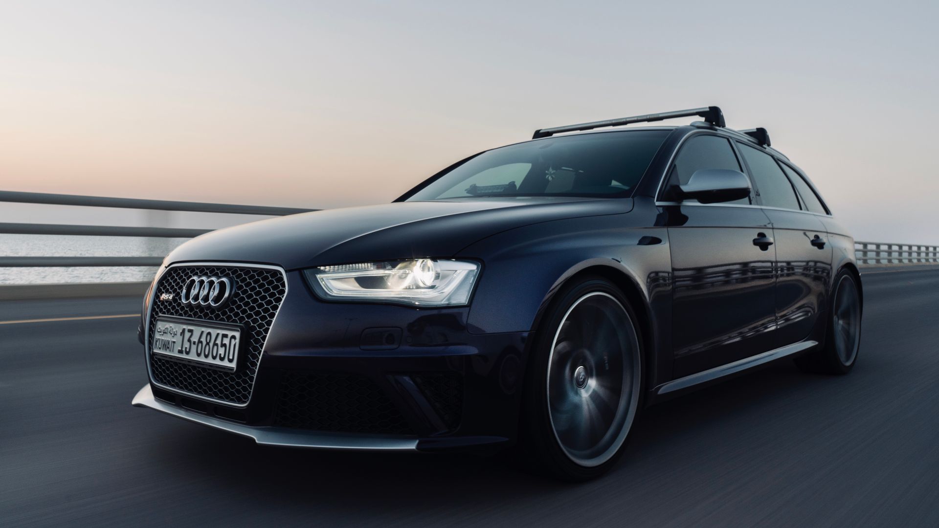 A sleek black Audi car driving on a highway during golden hour sunset