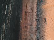 Overhead view of dark wavy reservoir and sandy shore covered with long thin messy trails in sunlight