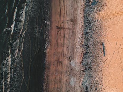 Overhead view of dark wavy reservoir and sandy shore covered with long thin messy trails in sunlight