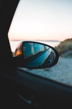 View from inside transport with side mirror on coast near ocean at sundown
