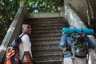 Friends in casual clothes with backpacks with hiking equipment going upstairs in green park in daytime