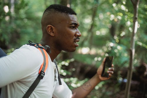 Black man with backpack and smartphone in forest