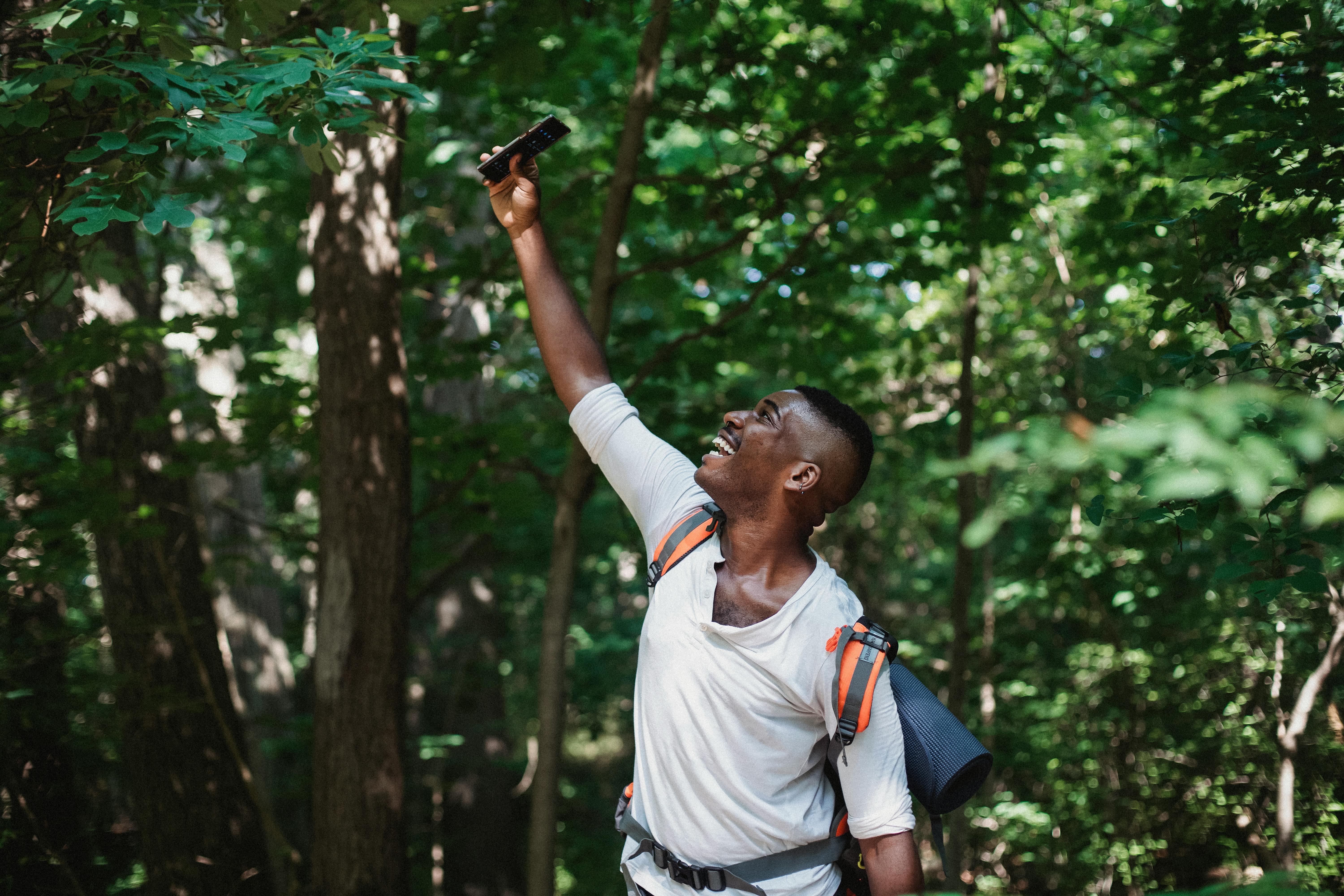 Happy African American male with backpack and mobile phone finding connection during hiking