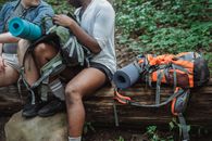 Faceless hikers checking big rucksack in forest