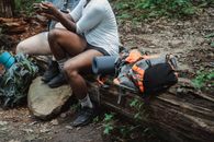 Unrecognizable adventurers lounging on old dark brown weathered log and surfing internet in forest in daytime