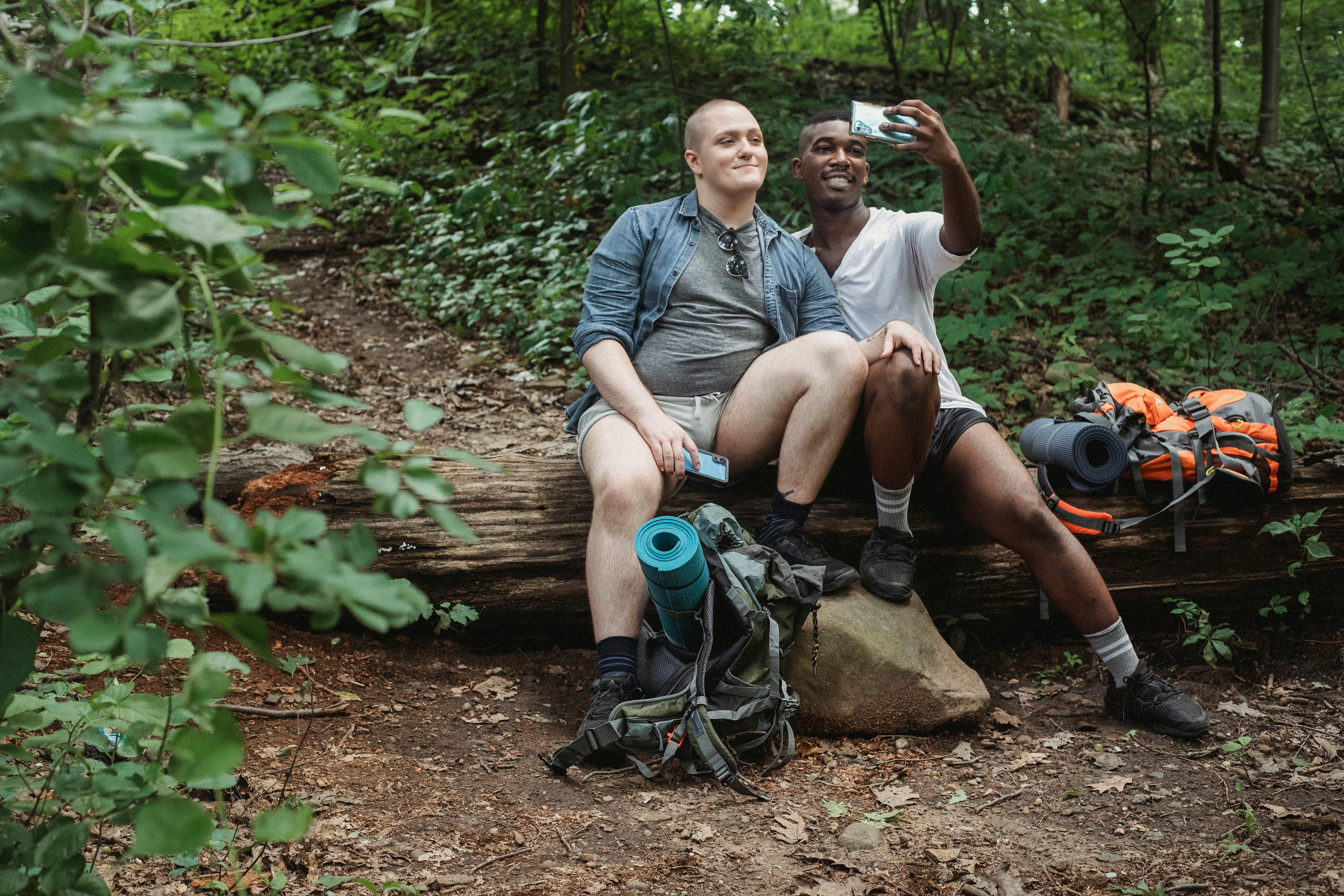 traveling gay couple taking selfie on log in forest