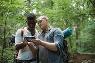 Focused multi ethnic backpackers watching smartphone while finding location in woodland in daytime on blurred background