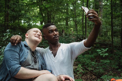 Gay couple hugging and taking selfie in forest