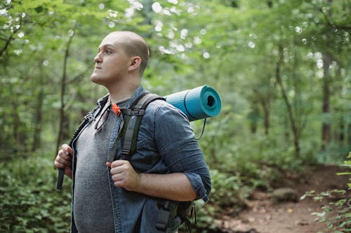 Male plump backpacker with hiking equipment in woods