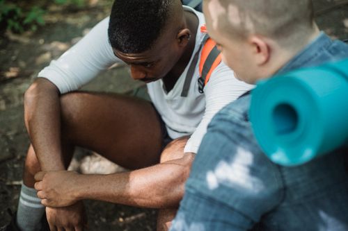 Free From above of tired African American male hiker having break in trekking with friend in woods Stock Photo