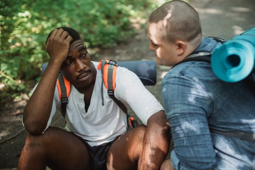Free From above of tired African American male hiker talking to friend about problem while hiking together Stock Photo