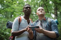 From below of diverse lost travelers with backpacks exploring woodland and searching way in cellphone