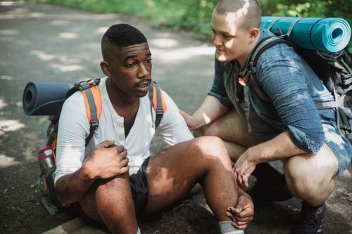 Free High angle of tired African American male tourist talking to friend while having break in difficult route in wildlife Stock Photo