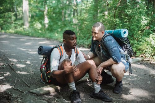 Free Full body of tired African American male traveler sitting on ground with friend during difficult trekking Stock Photo