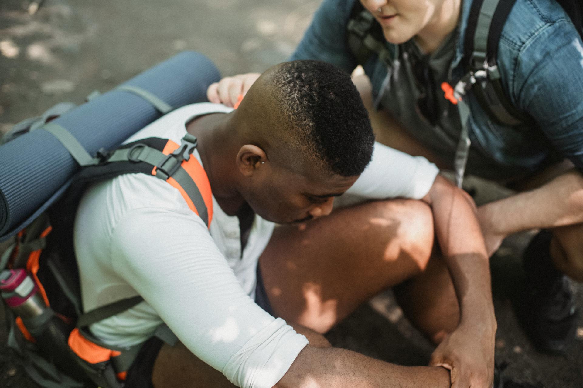 From above of man supporting tired African American friend exhausted while trekking in wildlife