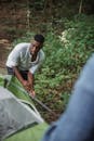 Handsome African American male hiker in activewear standing in green forest and putting tent