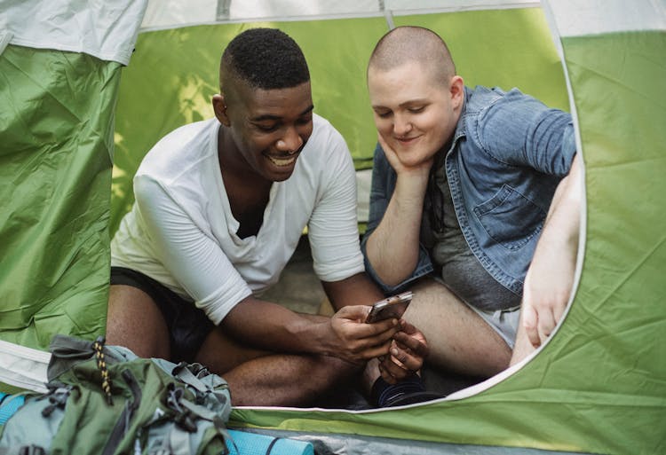 Laughing  Man Showing Smartphone To Friend In Tent