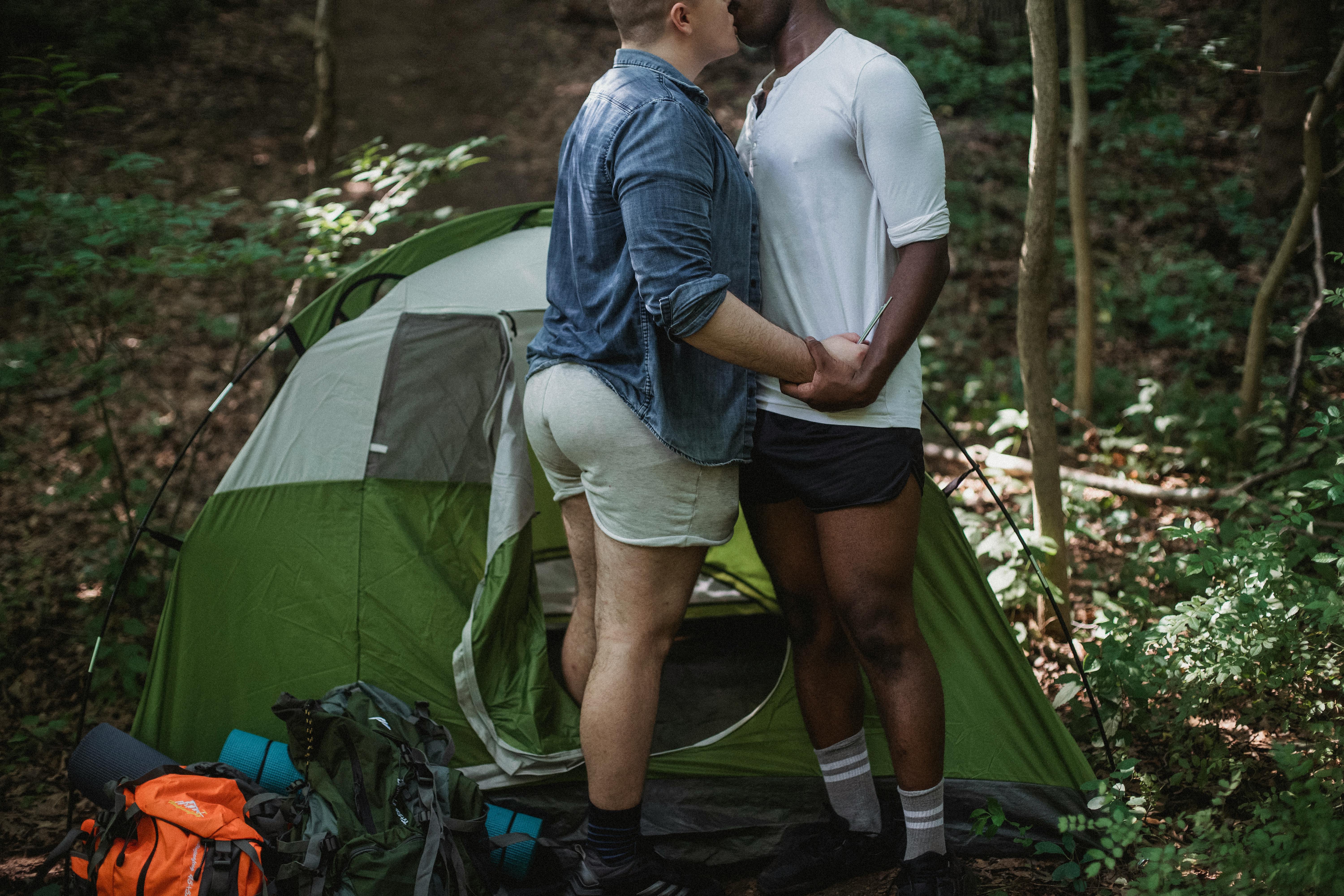 счастливая гей пара целуется возле палатки в лесу · Бесплатные стоковые фото
