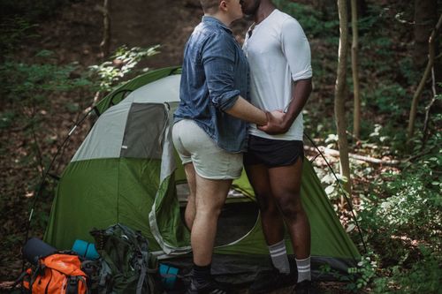 Free Crop of unrecognizable multiracial gay couple kissing on nature during summer vacation in forest in green tent Stock Photo