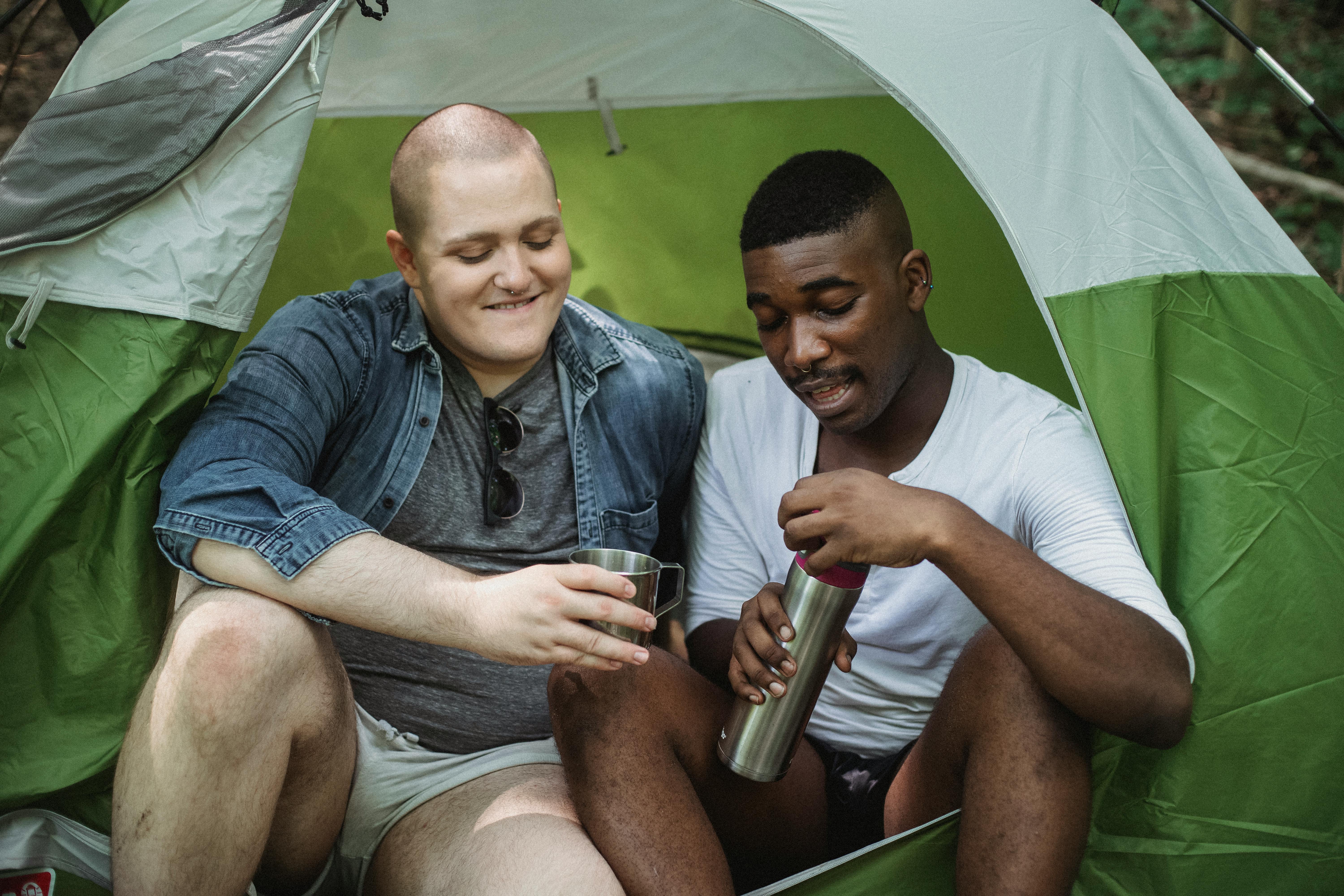 cheerful men with thermos resting in tent