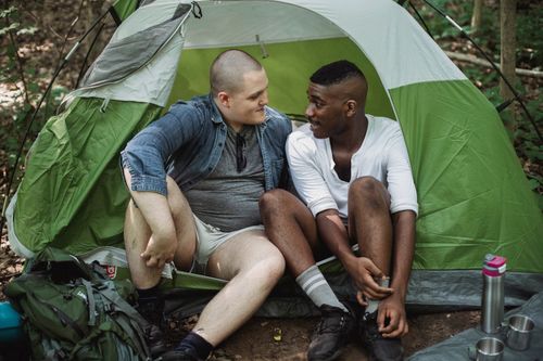 Free Positive young multiracial hikers resting in camping tent while spending time together in nature Stock Photo