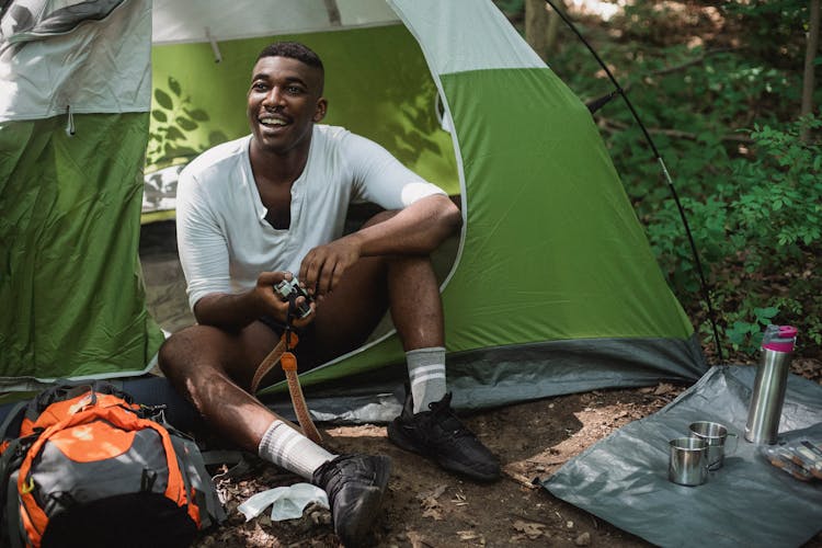 Happy Black Man Relaxing In Tent In Forest