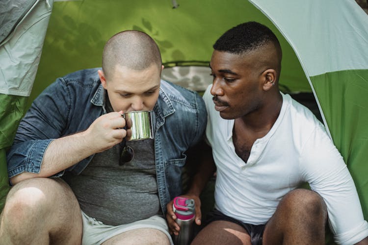 Man Drinking Tea From Thermos Sitting With Black Friend