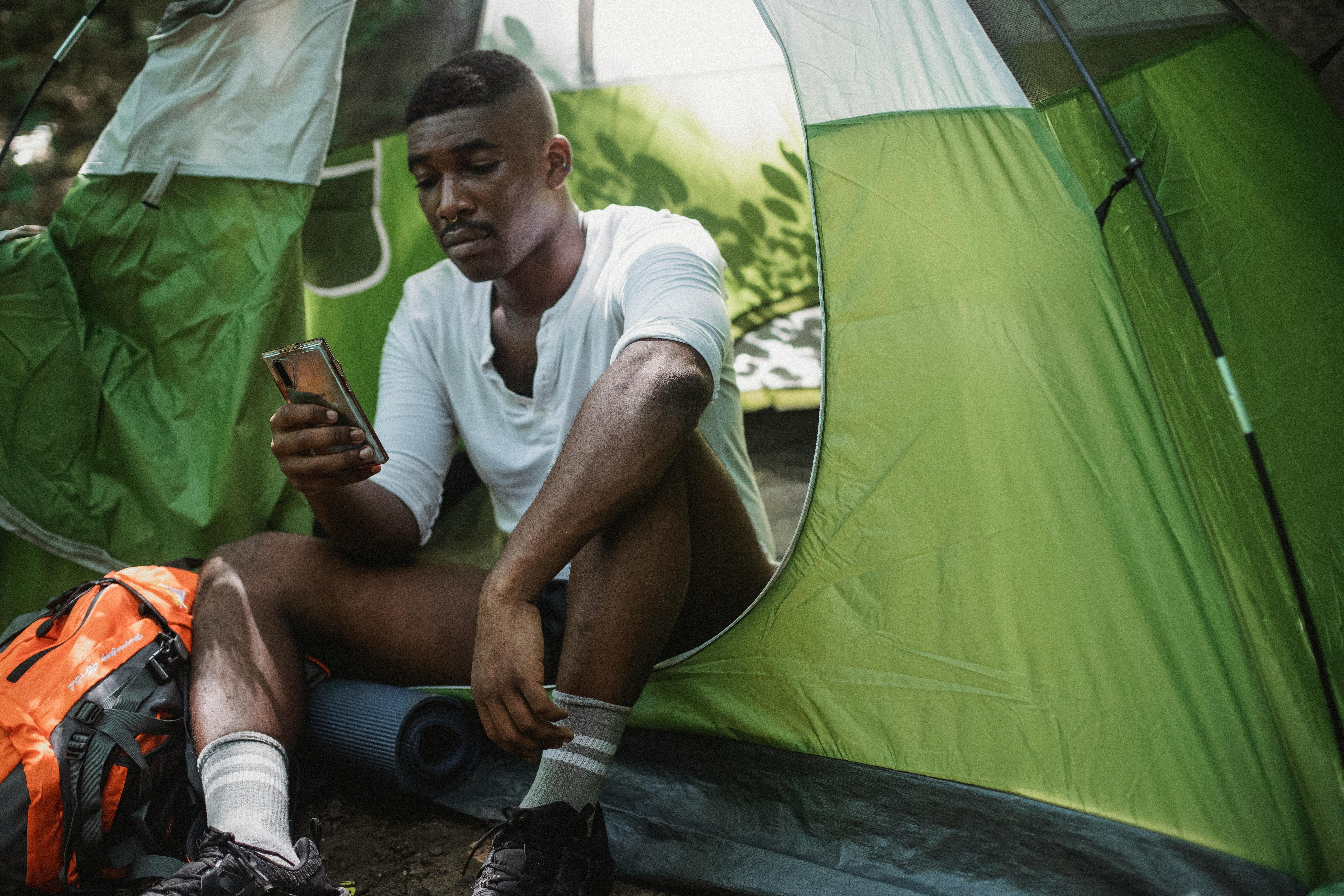 unhappy black man surfing smartphone in tent