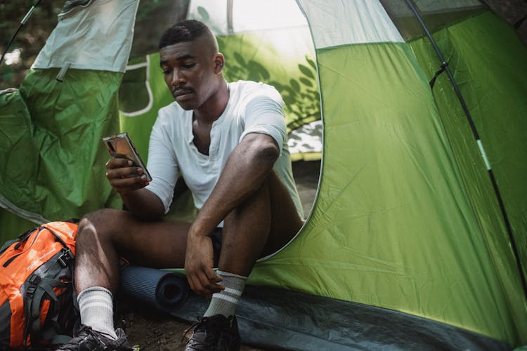 Unhappy Black Man Surfing Smartphone In Tent