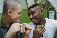 Positive multiethnic same sex couple drinking tea in tent