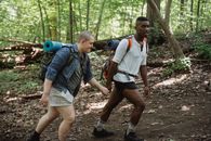 Same sex diverse couple with trekking equipment holding hands while traveling in forest