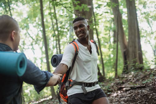 African American hiker helping man to climb up