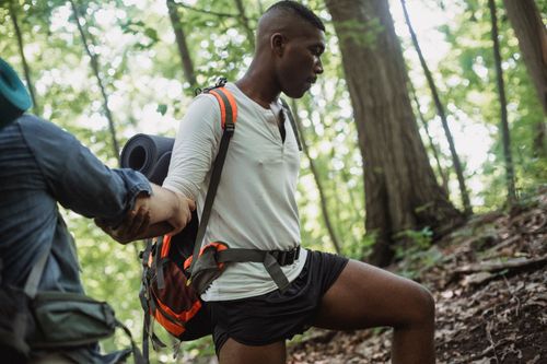 Free Unrecognizable male tourist holding elbow of black young friend with backpack while trekking in summer forest Stock Photo