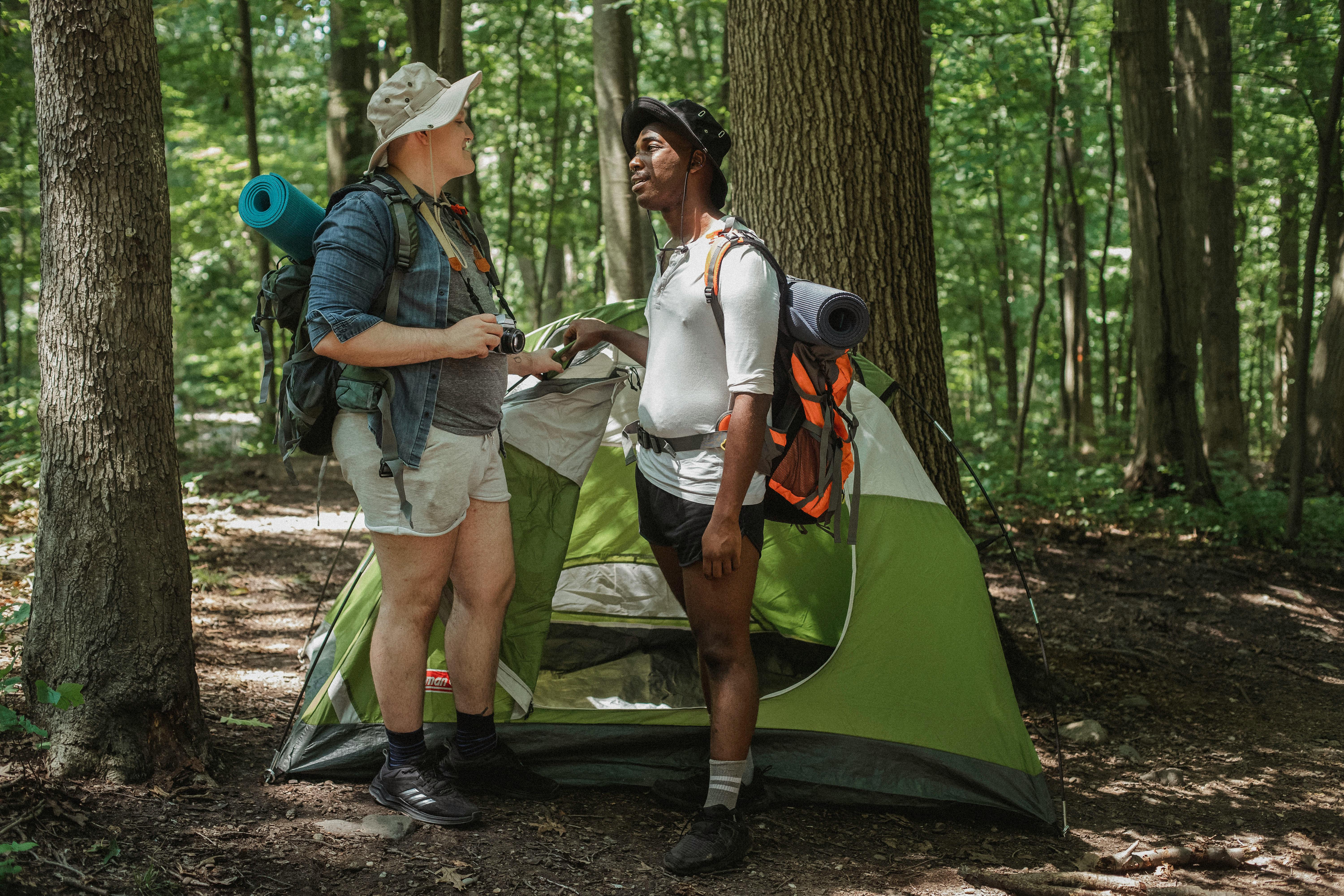 male friends with backpacks near tent in woods