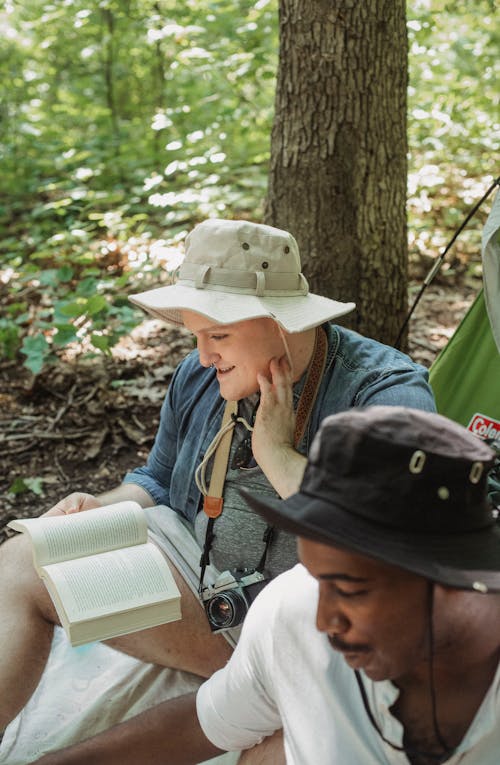 Smiling tourists in safari hat with books resting and enjoying nature in forest in sunny day