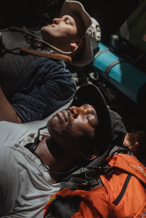 Diverse male hikers sleeping on rucksacks on weekend